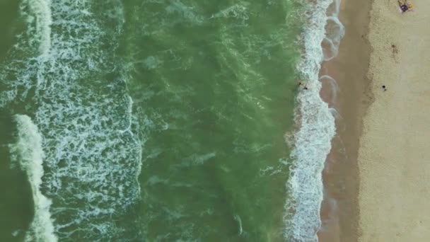 空中ドローンは緑色のターコイズブルーの水と泡の波がビーチを飛び回るのを見る。夫婦で海に泳ぎに行き — ストック動画