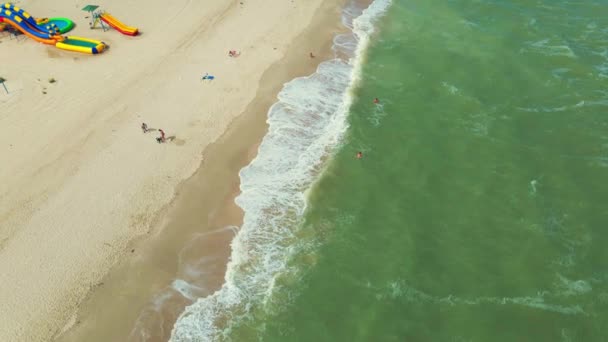 リゾートや太陽の傘やビーチのアトラクションと砂浜の海辺への空中の視点. — ストック動画