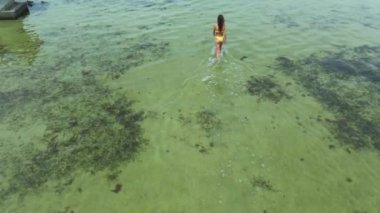 Yavaş çekim drone görüntüsü. Sarı bikinili kadın denize giriyor.