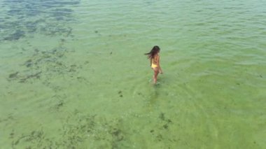 Yavaş çekim drone görüntüsü. Sarı bikinili kadın denize giriyor.