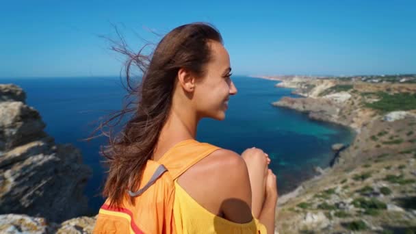 Vrouw zitten op top rock strand, helder gele jurk en haar waait in de wind. — Stockvideo