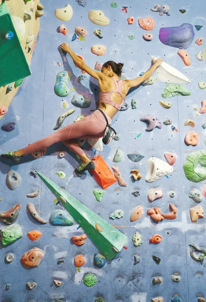 Starke Bergsteigerin mit muskulösem Körper klettert in Boulderhalle an Wand. — Stockfoto