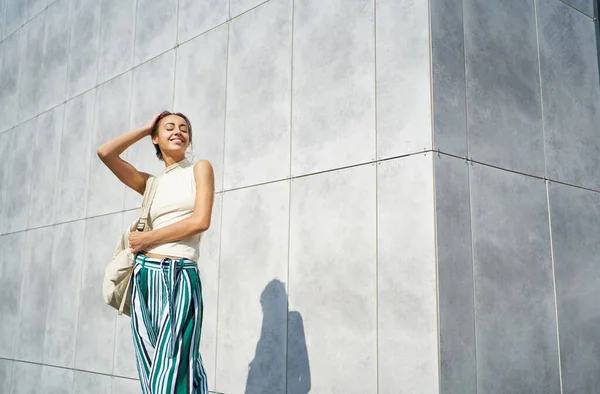 Привлекательная женщина-модель улыбается и позирует над серой бетонной стеной на улице — стоковое фото