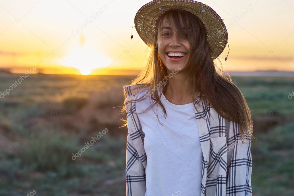Emotional portrait happy hipster woman on sunset in nature view. Hipster treveler girl in hat in golden sun rays