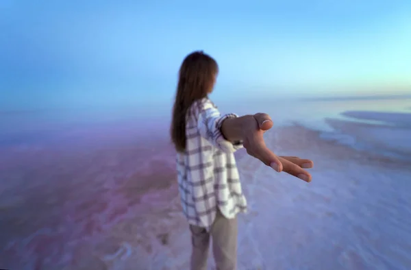 Brunettekvinne i bakspeilet strekker ut en hånd til kamera, går forbi en vakker, rosa sjø.. – stockfoto