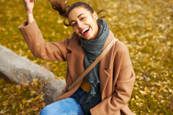 Syksyn muotokuva tyylikäs nainen takki hymyilee ja nauraa, istuu ruoho värikkäitä lehtiä — kuvapankkivalokuva