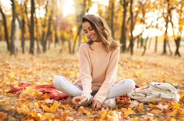 Pretty woman in cozy sweater in autumn park with fall colorful background, sitting on blanket. — Stock Photo, Image