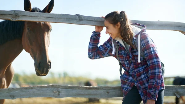 Delighted woman in casual coat on countryside enjoying time at farm or ranch, looking at horse — Stock Photo, Image