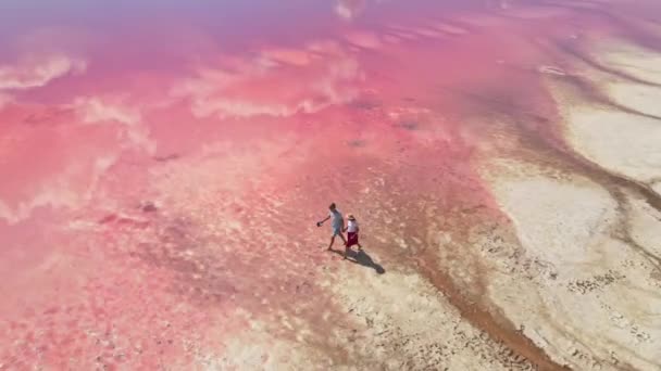 Půvabný mladý pár kráčí podél krásného růžového jezera se slaným břehem — Stock video