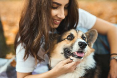 Evcil Galli Corgi köpeğiyle yakın plan portresi yapan kadın. Arka planda düşmüş turuncu yapraklar.