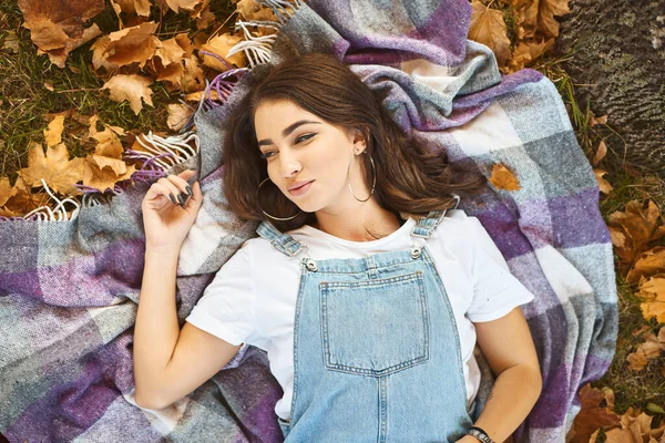 Mooie stijlvolle vrouw liggend op gezellige deken in een park, kleurrijke gevallen bladeren rond. — Stockfoto