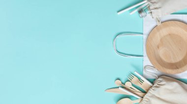 Sıfır atık plastik set ahşap çatal bıçak, kağıt torba, cam şişe, pipet içme, mavi arka planda market poşeti. Kopyalama alanı olan üst görünüm. Kavram - çevre dostu sıfır atık plastik. Banne.