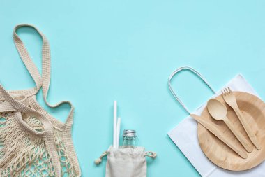 Sıfır atık plastik set ahşap çatal bıçak, kağıt torba, cam şişe, pipet içme, mavi arka planda market poşeti. Kopyalama alanı olan üst görünüm. Kavram - çevre dostu sıfır atık plastik.