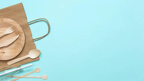 Zero waste plastic free set with wooden cutlery, paper bag, glass bottle, drinking straws and wooden sticks for stirring on blue background. Top view with copy space. Concept - environmentally friendly zero waste plastic free.