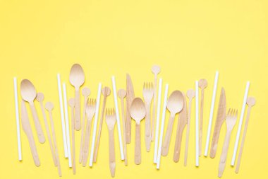 Ahşap çatal bıçak seti ve sarı arka plana saçılmış beyaz kağıt kamışlar. Ekolojik ürün. Tek kullanımlık ekipmanlar. Plastik alternatif. Sıfır atık