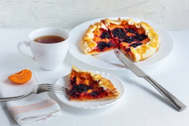Kayısı turtası ve siyah frenk üzümü. Beyaz arka planda yaz meyveli dalette. Lezzetli olgun meyve tatlısı. Ev yapımı pişirme. Seçici odaklanma. Kapat..