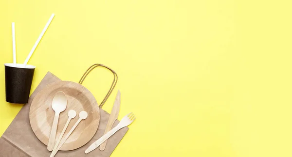 Zero waste plastic free set with wooden cutlery, paper bag and cup, drinking straws and wooden sticks for stirring on yellow background. Top view with copy space. Concept - environmentally friendly zero waste plastic free. Banne