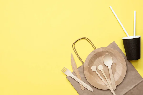 Zero waste plastic free set with wooden cutlery, paper bag and cup, drinking straws and wooden sticks for stirring on yellow background. Top view with copy space. Concept - environmentally friendly zero waste plastic free.