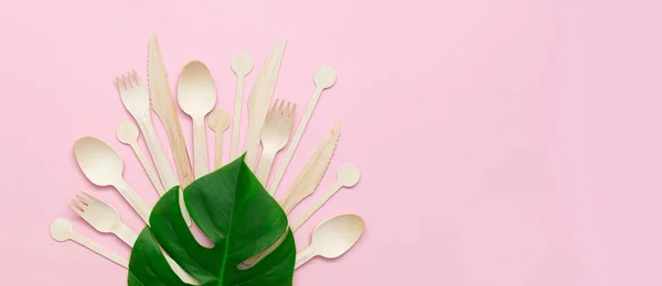 Zero waste plastic free set with wooden cutlery, wooden sticks for stirring and leaf Monstera palm on pink background. Top view with copy space. Concept - environmentally friendly zero waste plastic free. Banne