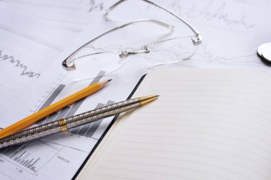 Grafikler ve okla ilgili mali rapor. Kalem, kalem, gözlük, defter ve finansal belgeler. İş büyümesi ve Finans Konsepti. Seçici Odaklanma