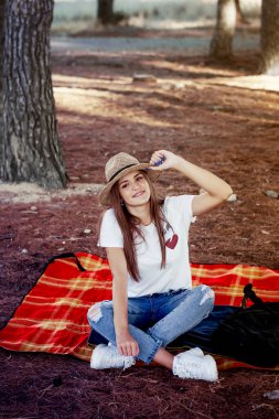 Gülümseme görüntüsü Bir sonbahar günü tarlada ekose battaniyede oturan şapkalı genç kadın