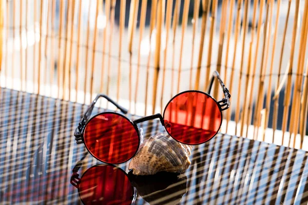 Okulary przeciwsłoneczne steampunk z czerwonym okrągłym obiektywem pozostają na stole w słoneczny dzień w lecie. Skupienie selektywne — Zdjęcie stockowe