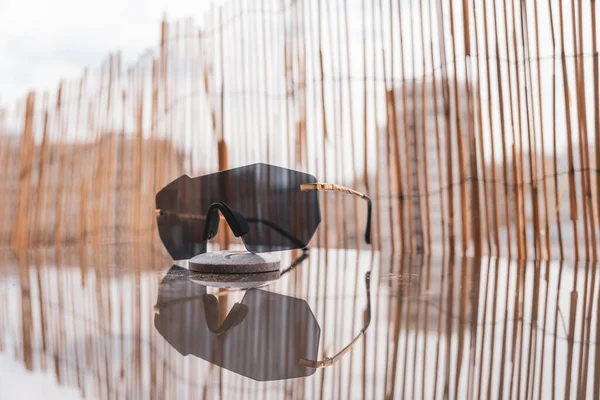 Futuristische zonnebril randloos design met zwarte lens op een tafel met bamboe omheining achtergrond. Selectieve focus — Stockfoto