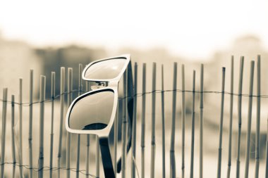 Metal çerçeveli ve bambu çitlere asılı siyah lensli klasik güneş gözlüğü. Seçici odak 