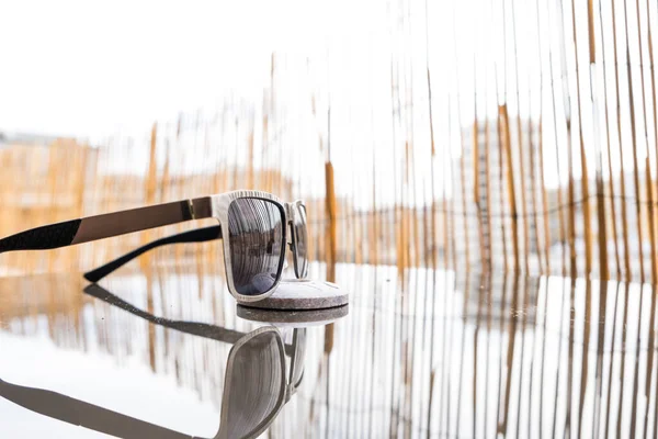 Κλασικό μοντέλο Sunglasses προφίλ με μεταλλικό σκελετό και μαύρους φακούς σε μια καλοκαιρινή μέρα με μπαμπού φράχτη στο παρασκήνιο. Επιλεκτική εστίαση — Φωτογραφία Αρχείου