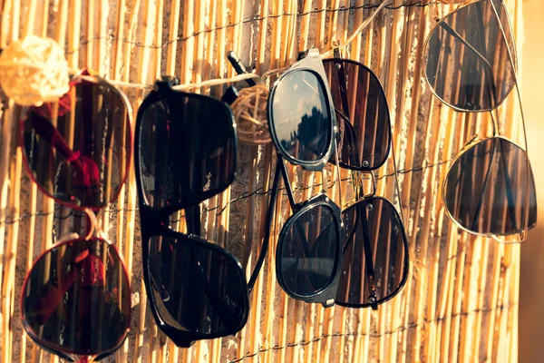 Colección de diferentes modelos de gafas de sol que reflejan la estancia del sol en una valla de bambú y esperando a ser elegidas en un día soleado. — Foto de Stock