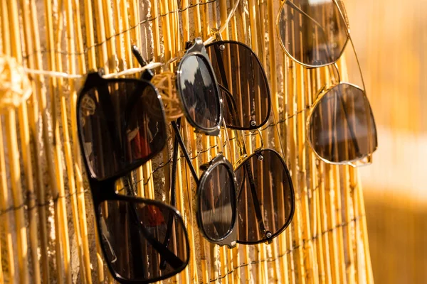 Collection of different sunglasses models reflecting the sun stay on a bamboo fence and waiting to be choose in a summer day.