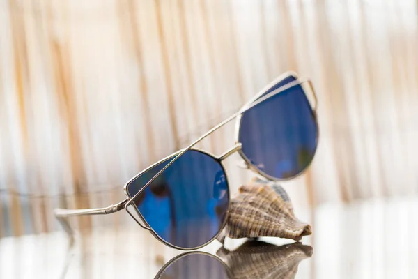 Olhos de gato óculos de sol modelo perfil para senhoras com lentes azuis ficar em uma concha refletindo o sol. Foco seletivo — Fotografia de Stock