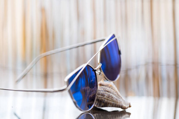 Cat eye sunglasses model profile for ladies with blue lenses stay on a shell reflecting the sun. Selective focus 