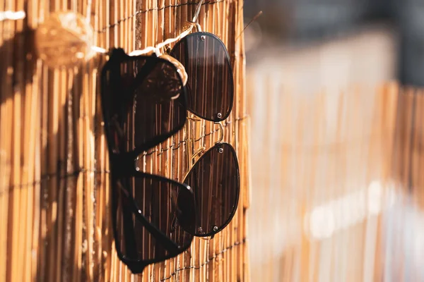 Collection of two different sunglasses models that stay on a bamboo fence in a summer day. Selective Focus — Stock Photo, Image