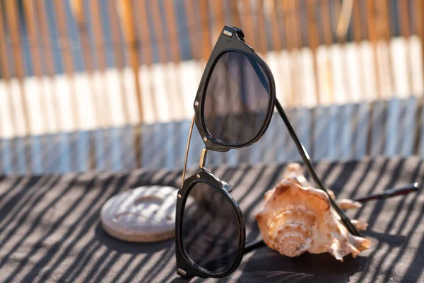 Czarne okulary przeciwsłoneczne, które pozostają na muszli w słoneczny dzień zbliżenia. Skupienie selektywne — Zdjęcie stockowe