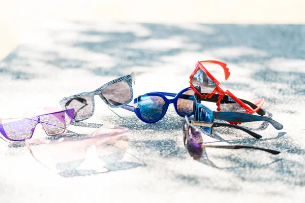 Colección de múltiples modelos de gafas de sol para hombres y mujeres se quedan en una mesa en un día soleado. Enfoque selectivo — Foto de Stock