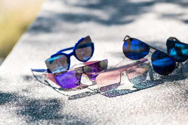 Collection of multiple sunglasses models for men and women stay on a table in a sunny day. Selective focus