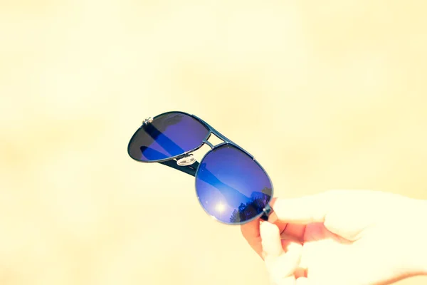 Модель ретро-авиатора в солнцезащитных очках держится вручную в летний день крупным планом. Селективный фокус — стоковое фото