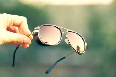 Kırmızı lensli retrogüneş gözlüğü modeli bir yaz günü doğada yakın plan çekimde el ele tutulur. Seçici odak