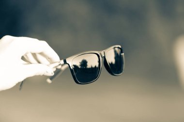 Siyah lensleri olan klasik bir güneş gözlüğü modeli. Bir yaz günü elle çekim yapıyor. Seçici odak