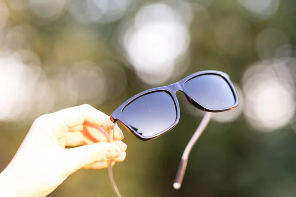 Modelo de gafas de sol clásicas con lentes negras sujetadas a mano en un día de verano. Enfoque selectivo — Foto de Stock