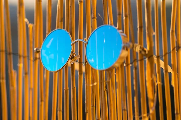Occhiali da sole Steampunk modello con lenti rotonde appese a una recinzione di bambù in un primo piano estivo. Focus selettivo — Foto Stock