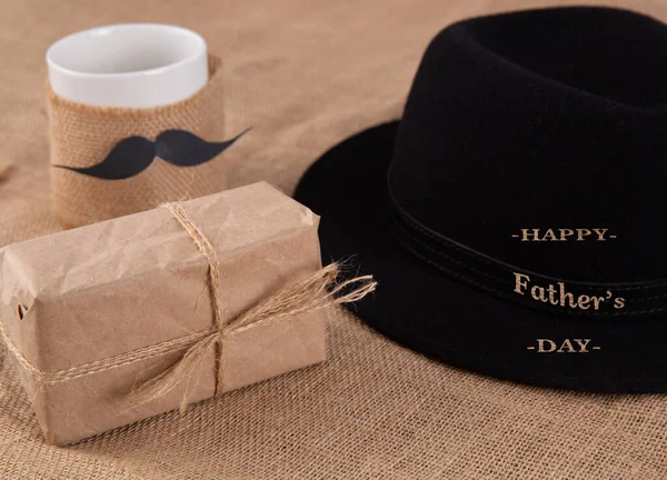 Gift box on the table. Next to a cup with a glued mustache. — Stock Photo, Image