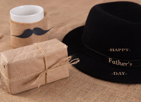 Geschenkdoos op tafel. Naast een beker met een verlijmde snor. — Stockfoto