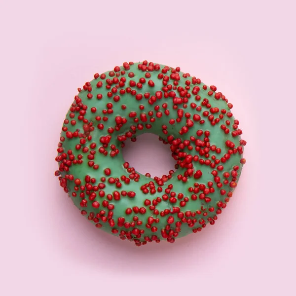 Beignet avec glaçage vert et boules de sucre sucré rouge. sur fond rose. — Photo