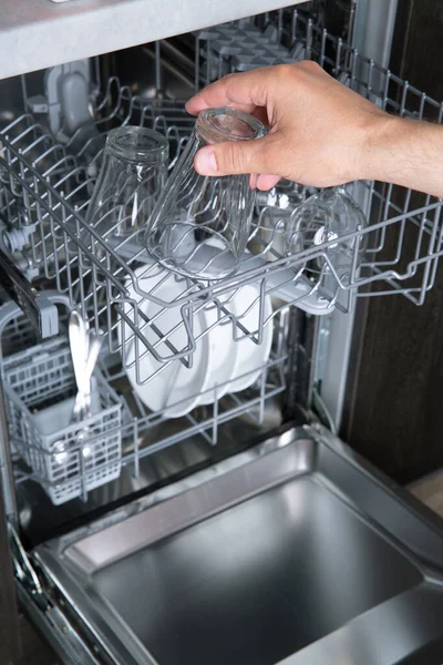 Hushållsarbete öppen diskmaskin och man sätta ett glas i maskinen — Stockfoto