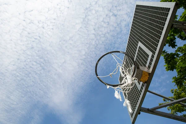 A broken basketball net dangles from a hoop attached to a metal backboard.