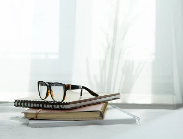 Un'immagine di un taccuino e libri collocati a letto con occhiali. Sfondo sfocato — Foto Stock