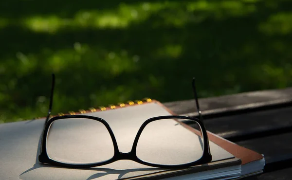 Glasses lie on top of a pile of books with a notebook on a bench in the park — Stock Photo, Image