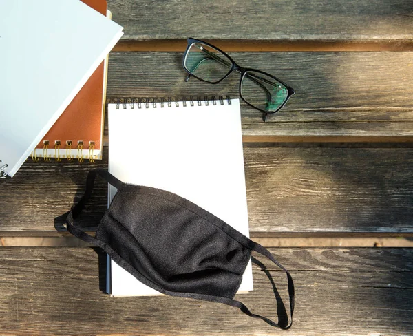 Maschera protettiva nera su notebook su una panchina di parco. — Foto Stock